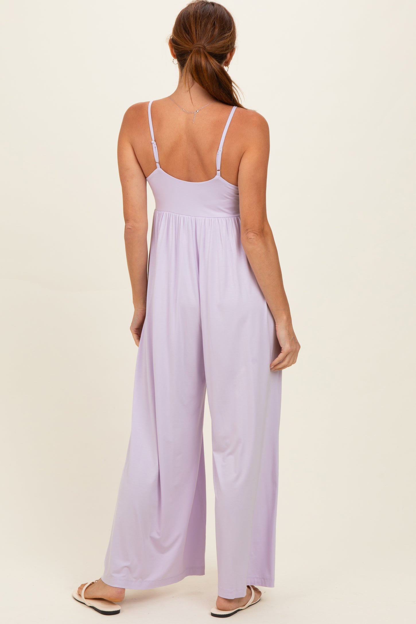 woman wearing a light purple sleeveless jumpsuit with a flowy wide leg design, shown from the back