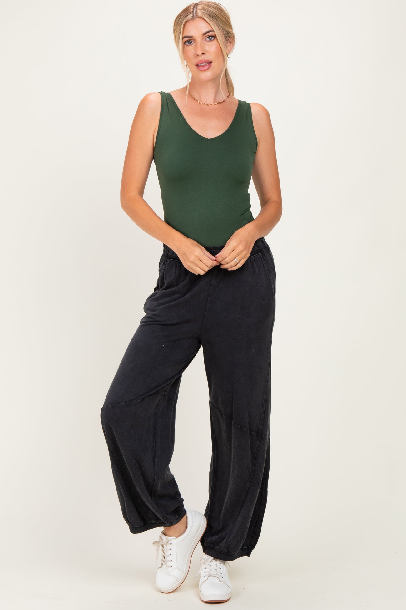 woman wearing a dark green fitted bodysuit and black loose-fitting pants, paired with white sneakers