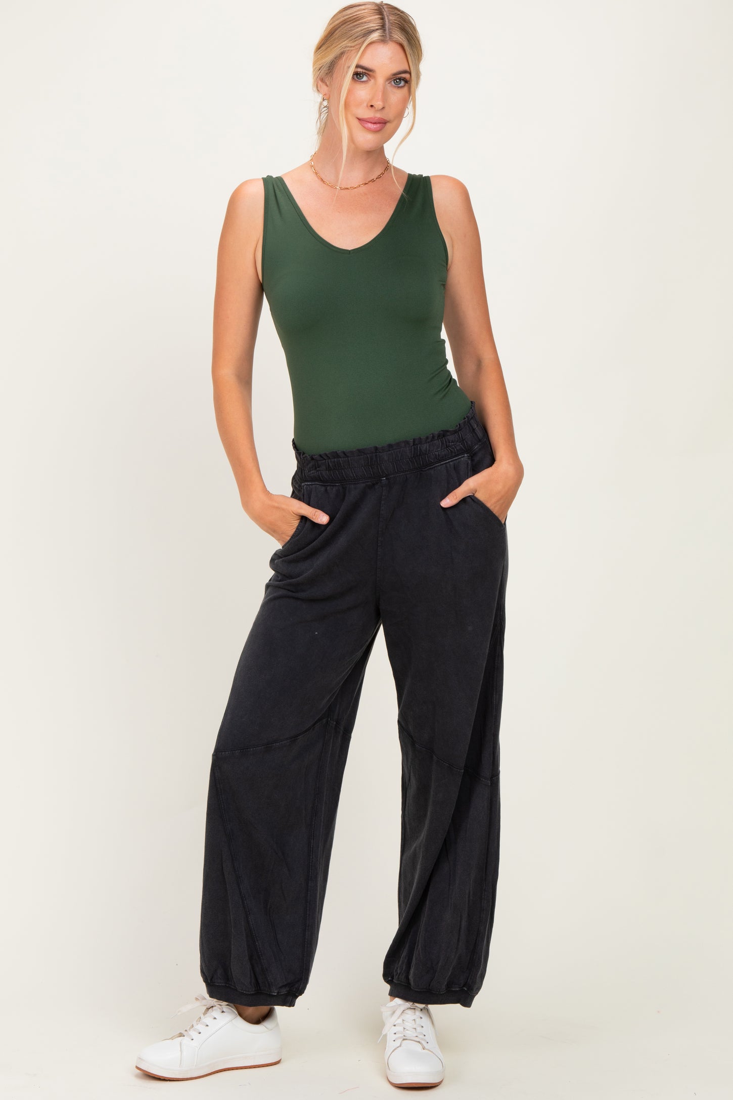 woman wearing a dark green sleeveless bodysuit and black comfy jogger pants with pockets, styled with white sneakers
