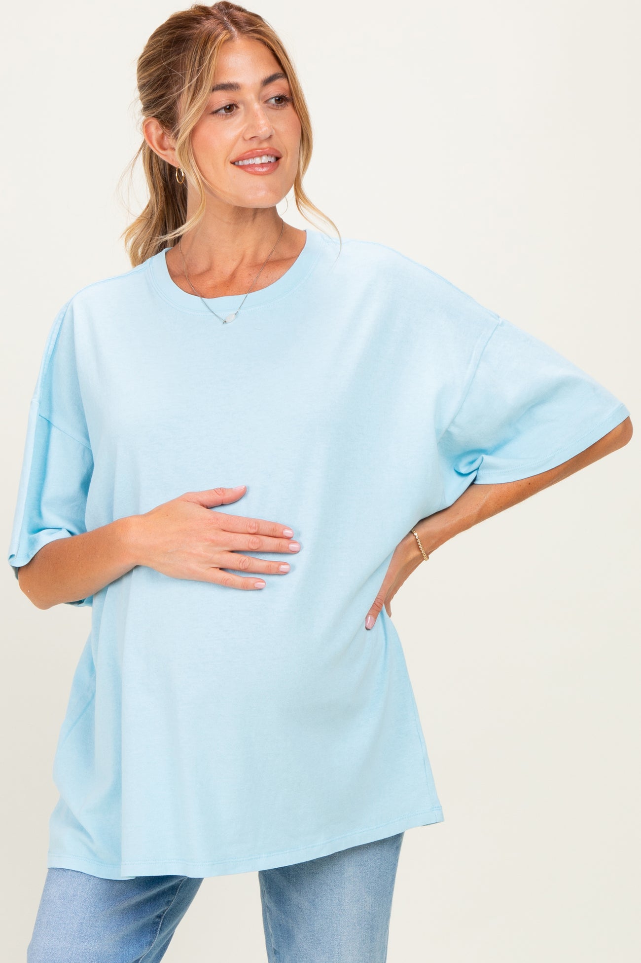 woman wearing a light blue oversized maternity t-shirt and holding her baby bump with a smile