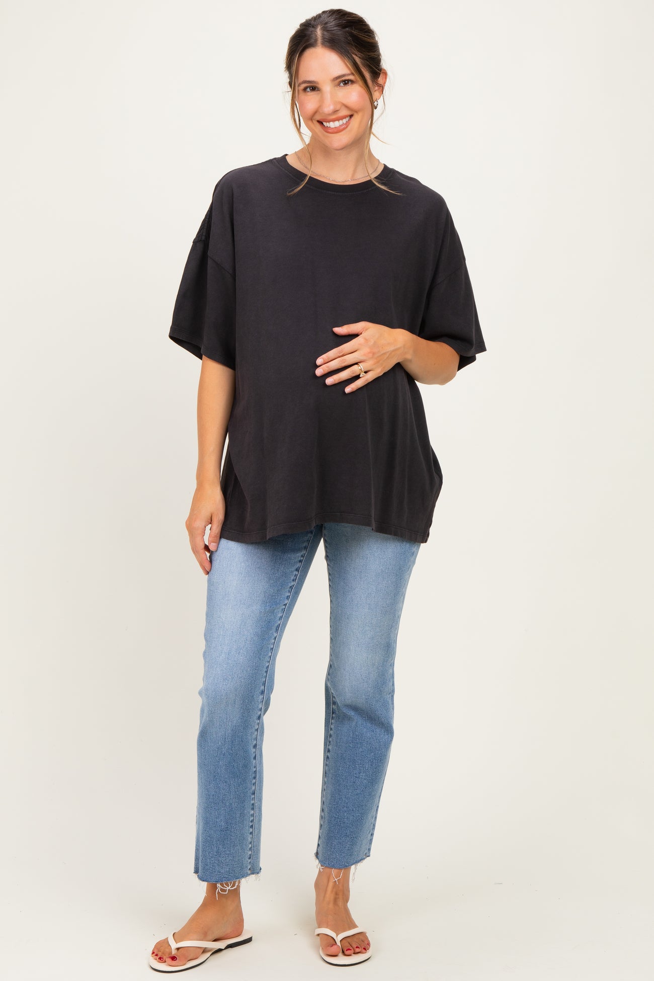 woman wearing a black oversized maternity top and light blue jeans, holding her baby bump