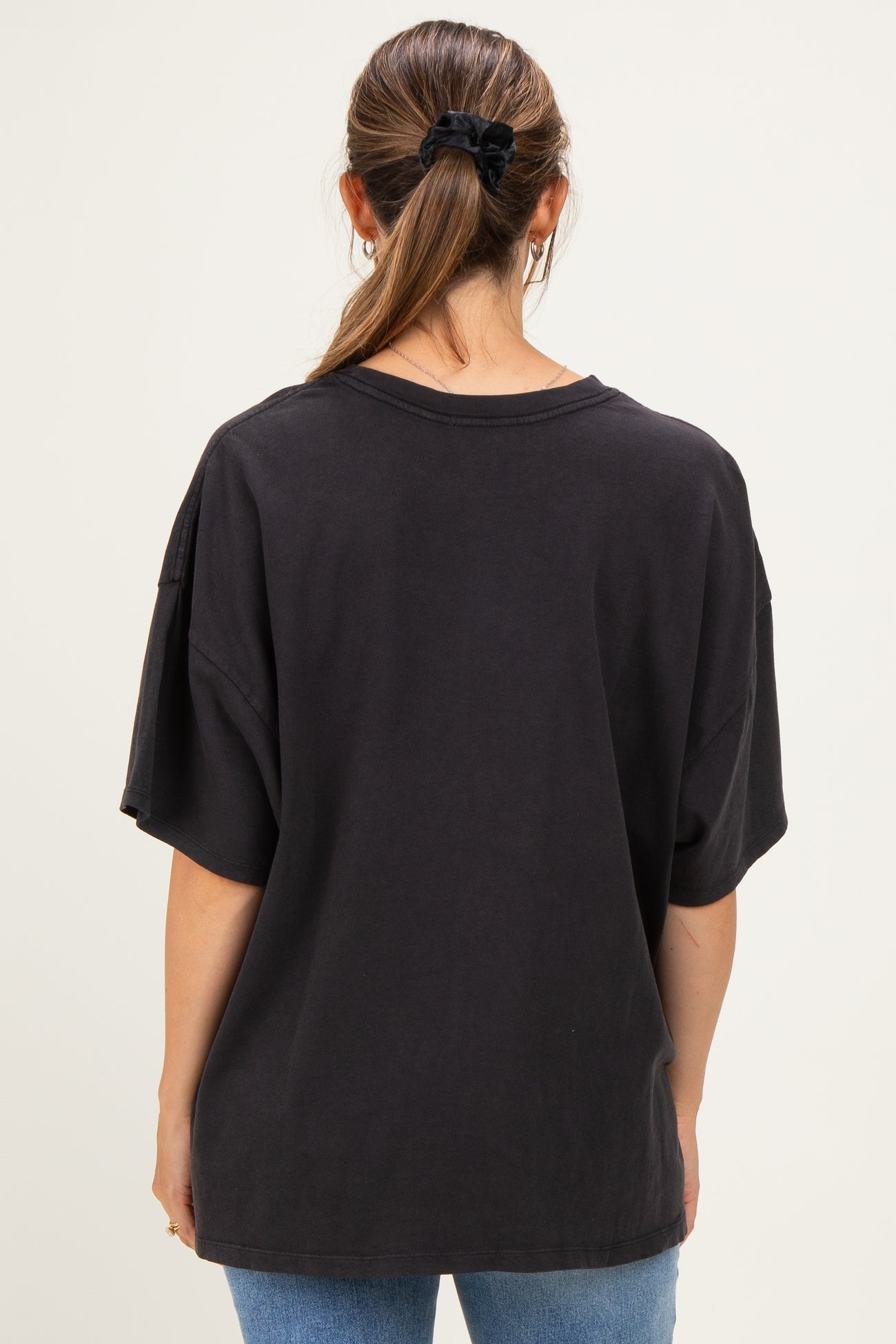 woman wearing a black oversized maternity t-shirt, seen from the back, paired with blue jeans