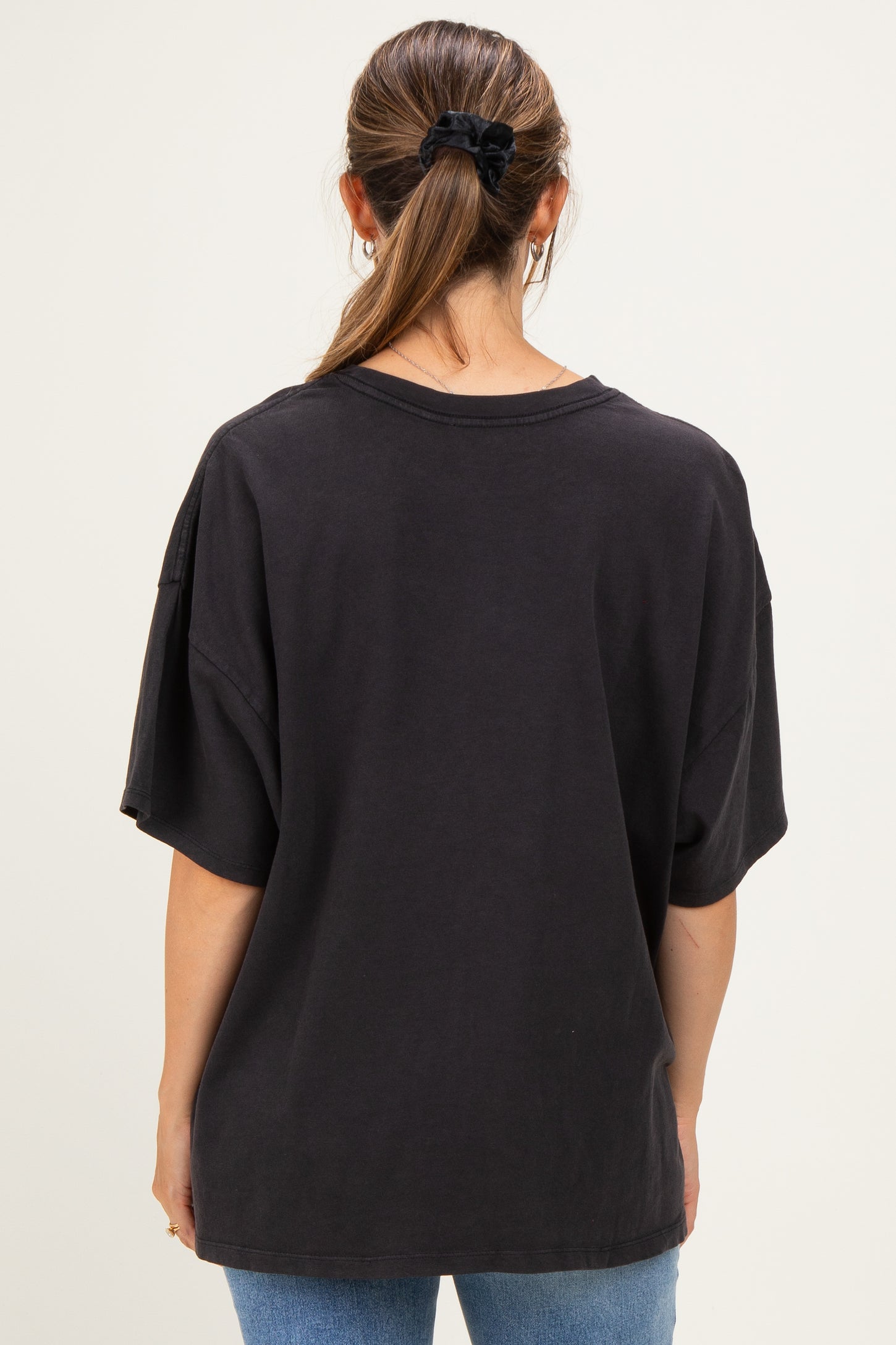 woman wearing a black oversized maternity t-shirt, seen from the back, paired with blue jeans