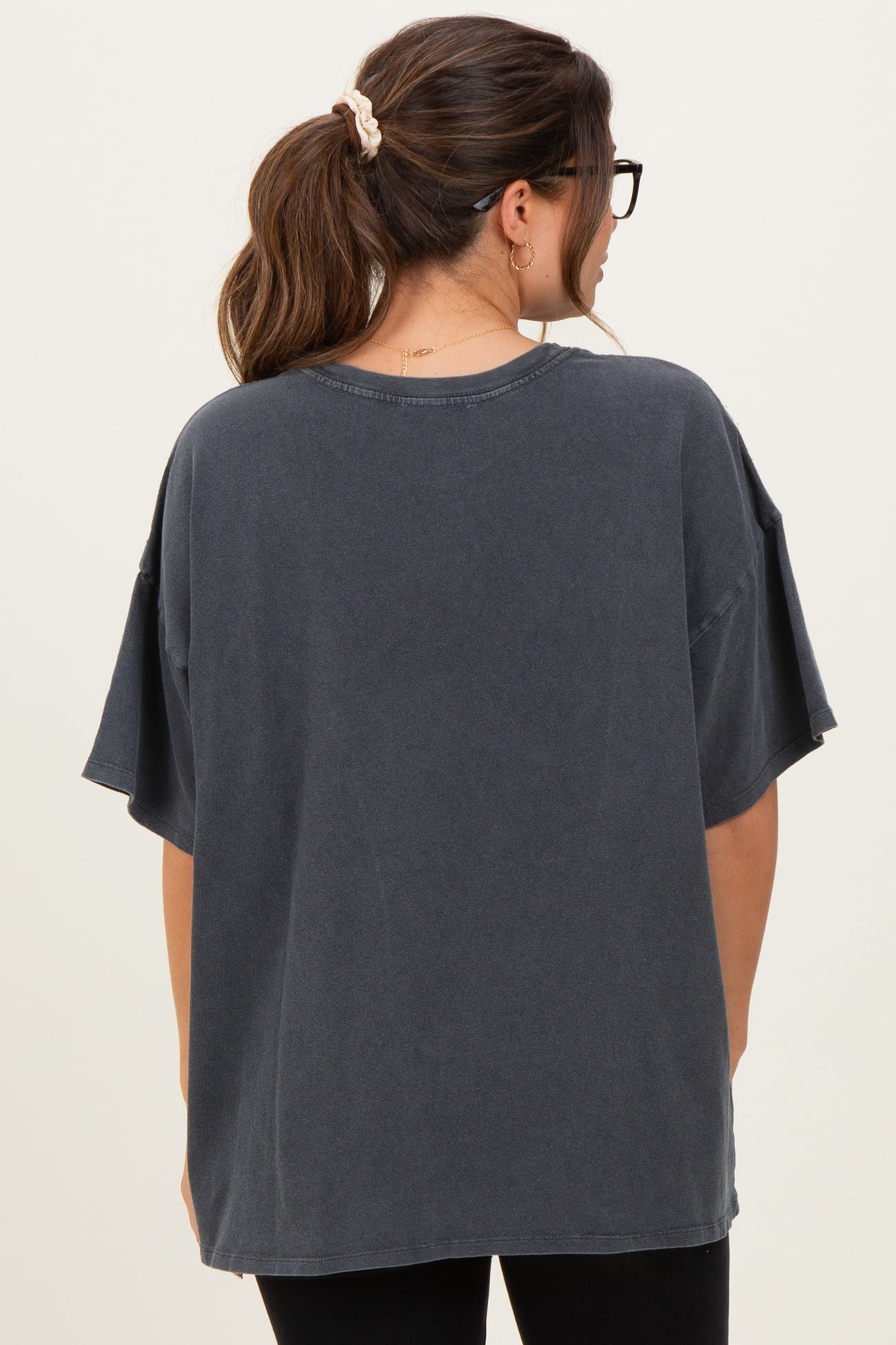 woman wearing a dark gray oversized maternity top with short sleeves, viewed from the back