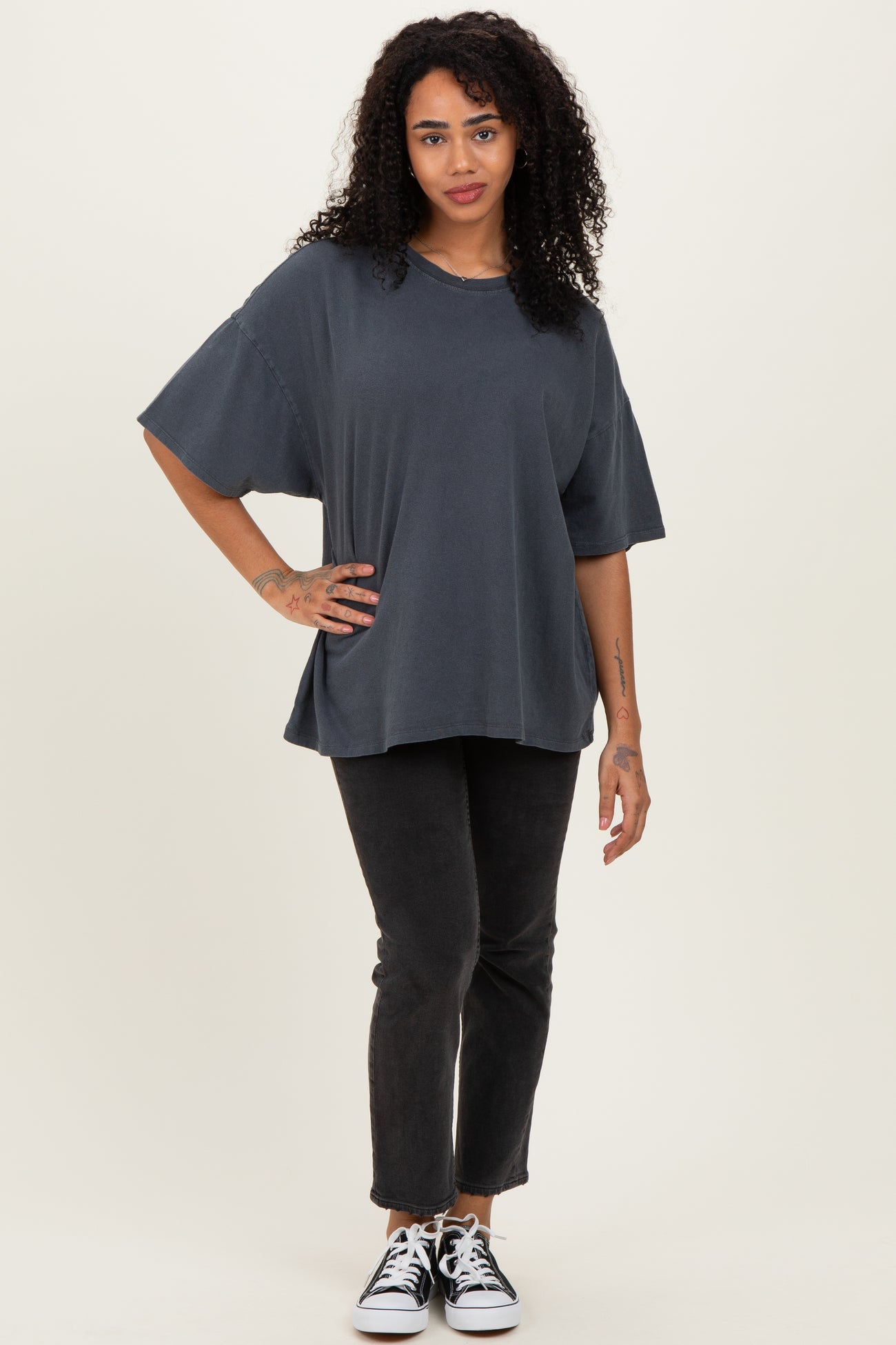 woman wearing a dark gray oversized short sleeve t-shirt and black skinny jeans with black and white sneakers