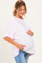 woman wearing a light pink oversized maternity t-shirt and holding her baby bump while smiling