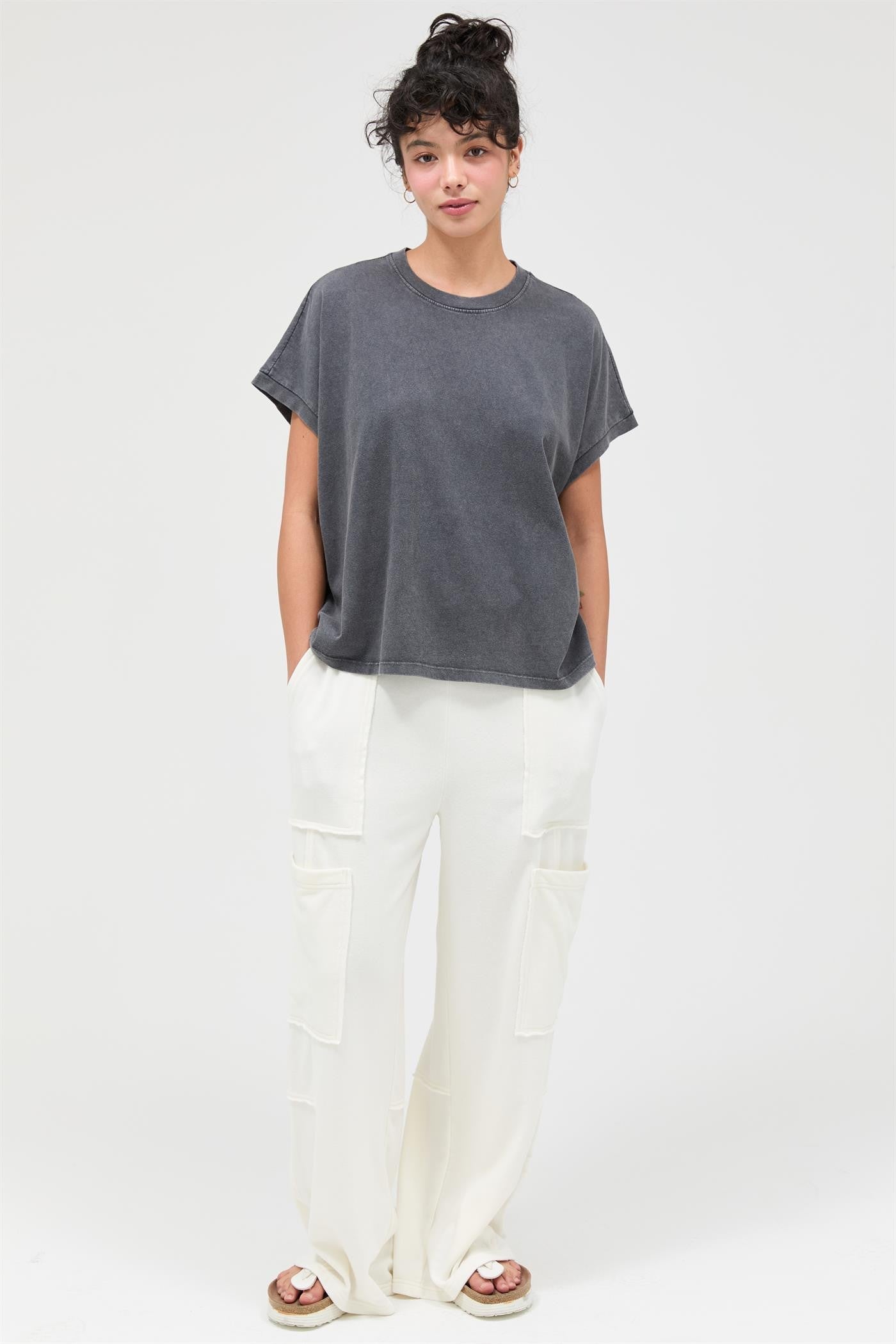 woman wearing a gray oversized t-shirt and white wide-leg trousers, standing against a plain background