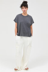 woman wearing a gray oversized t-shirt and white wide-leg trousers, standing against a plain background