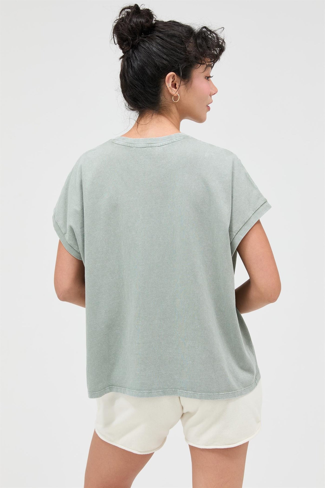 woman wearing a muted green oversized t-shirt and cream shorts, viewed from behind