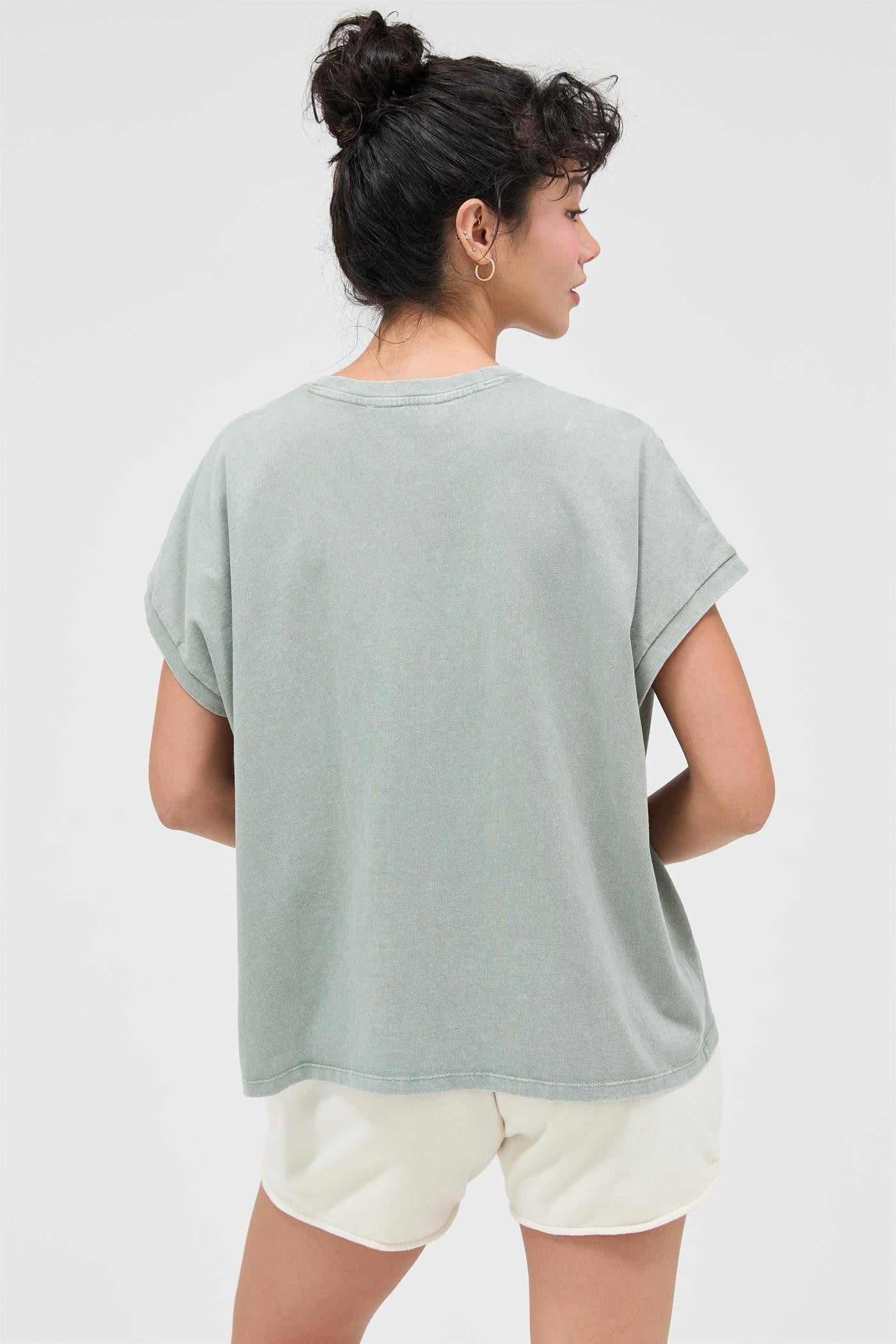 woman wearing a muted green oversized t-shirt and cream shorts, viewed from behind