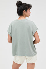 woman wearing a muted green oversized t-shirt and cream shorts, viewed from behind