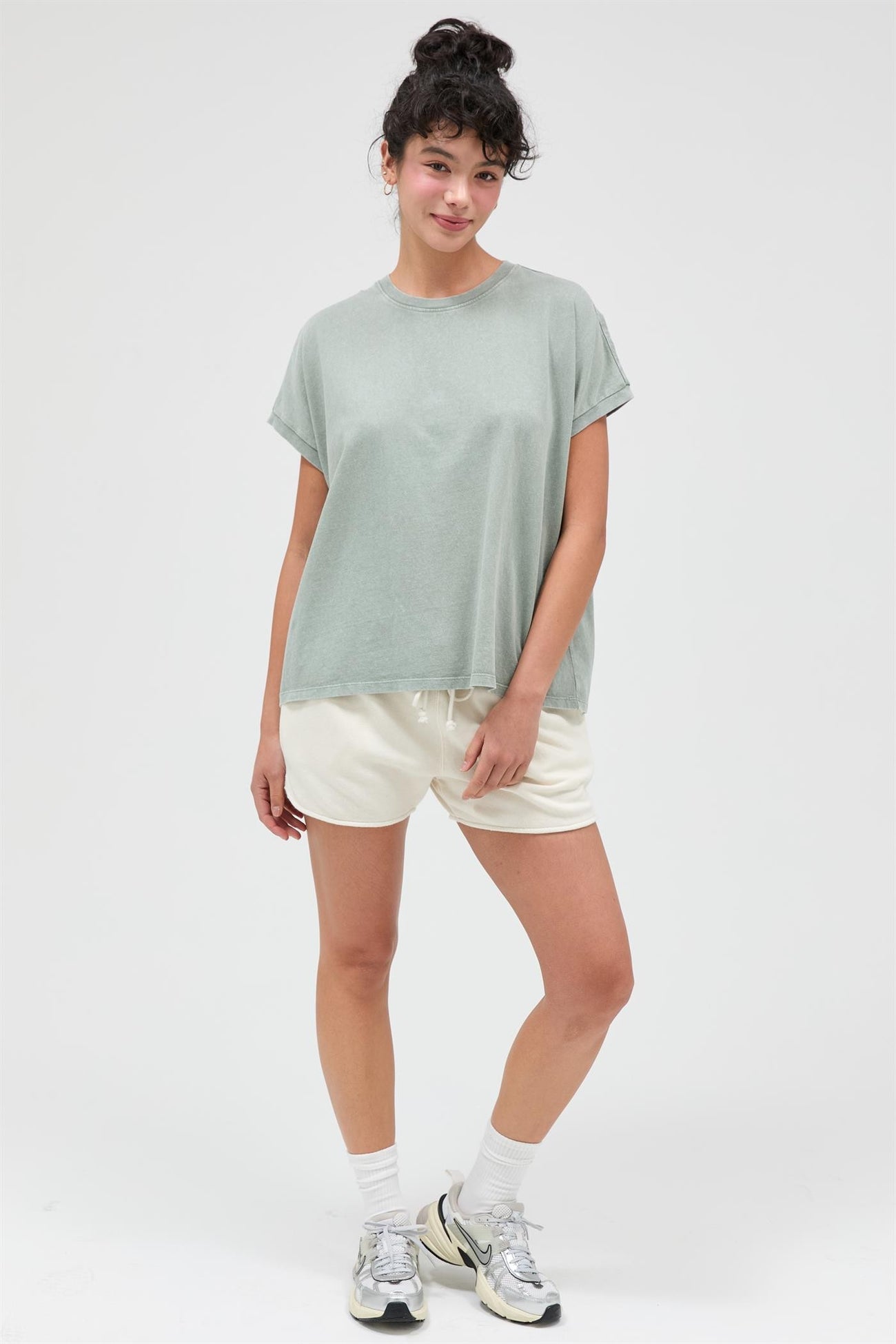 woman wearing a relaxed fit light green t-shirt and casual cream shorts, posing with hands on hips
