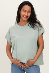 woman wearing a light green oversized maternity top and holding her baby bump