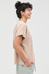 woman wearing a beige short sleeve t-shirt with rolled sleeves and smiling, styled with light green pants