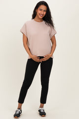 woman wearing a light pink maternity top and black pants, holding her baby bump