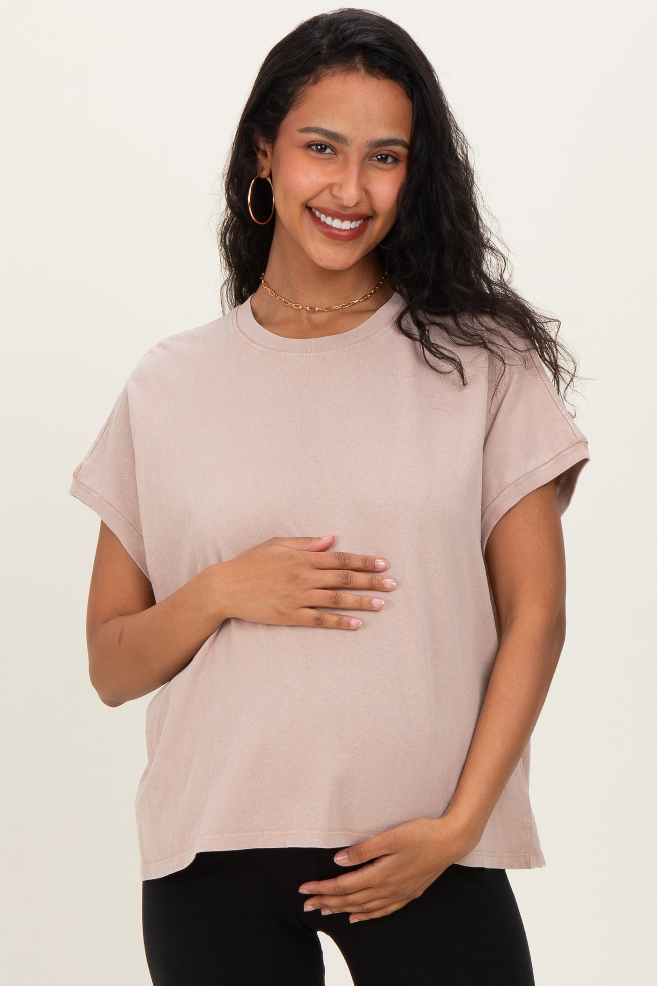 woman wearing a beige short sleeve maternity top and gently holding her baby bump