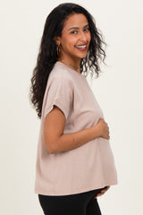 woman wearing a light pink maternity top and holding her baby bump, with a smile and curly hair