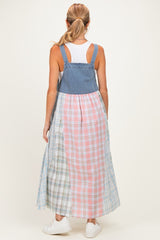 woman wearing a denim and plaid color block maternity dress with adjustable straps and a flowy skirt