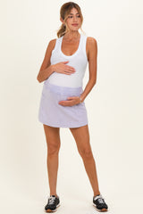 woman wearing a white tank top and a lavender maternity skort while holding her baby bump
