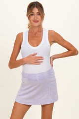 woman wearing a white tank top and a lilac maternity mini skirt, gently holding her baby bump