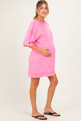 woman wearing a pink oversized maternity dress and cradling her baby bump