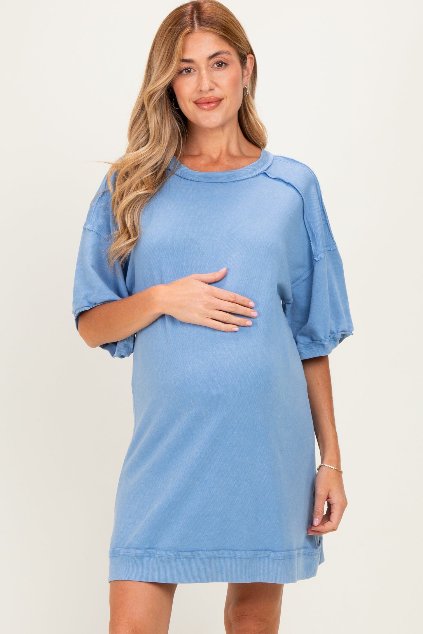 woman wearing a light blue maternity dress with oversized sleeves and holding her baby bump