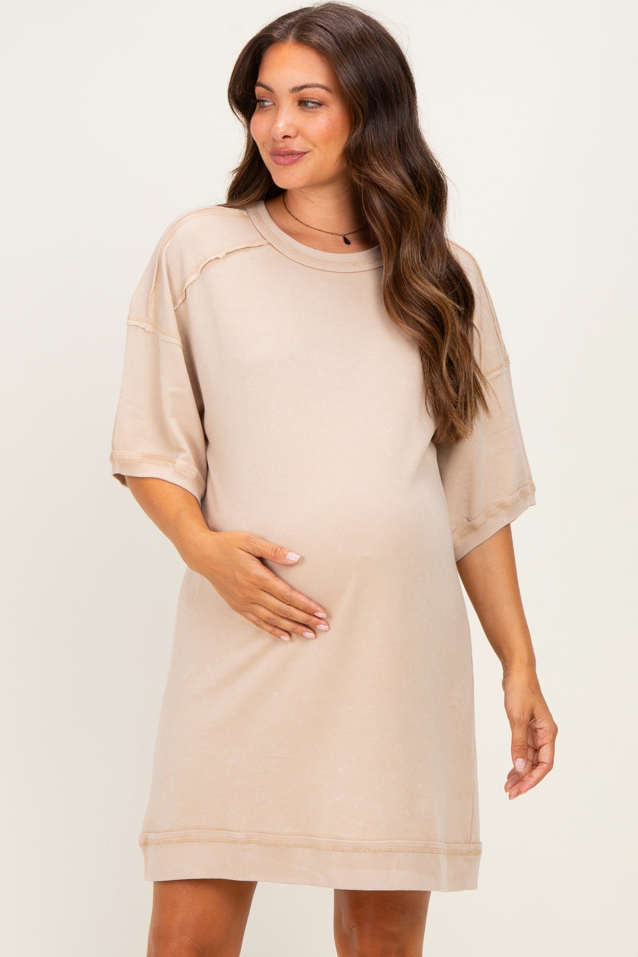 woman wearing a beige maternity short sleeve dress, gently holding her baby bump