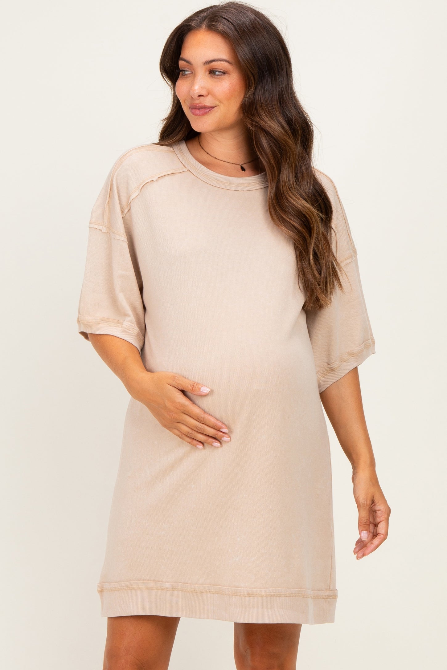 woman wearing a beige maternity short sleeve dress, gently holding her baby bump