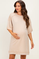 woman wearing a beige maternity short sleeve dress, gently holding her baby bump