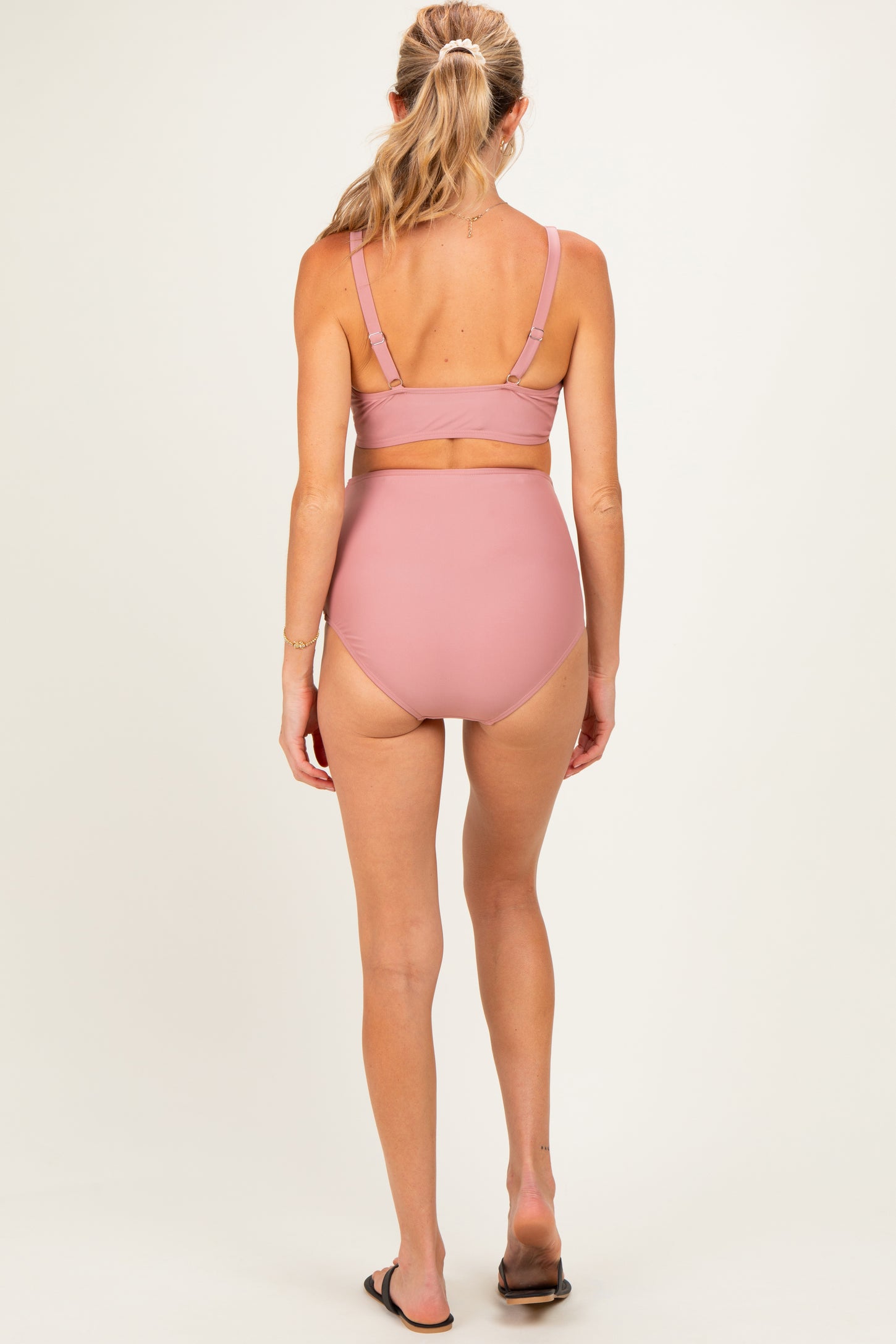 woman wearing a light pink maternity swim top and high-waisted bikini bottoms, showing her back
