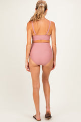 woman wearing a light pink maternity swim top and high-waisted bikini bottoms, showing her back