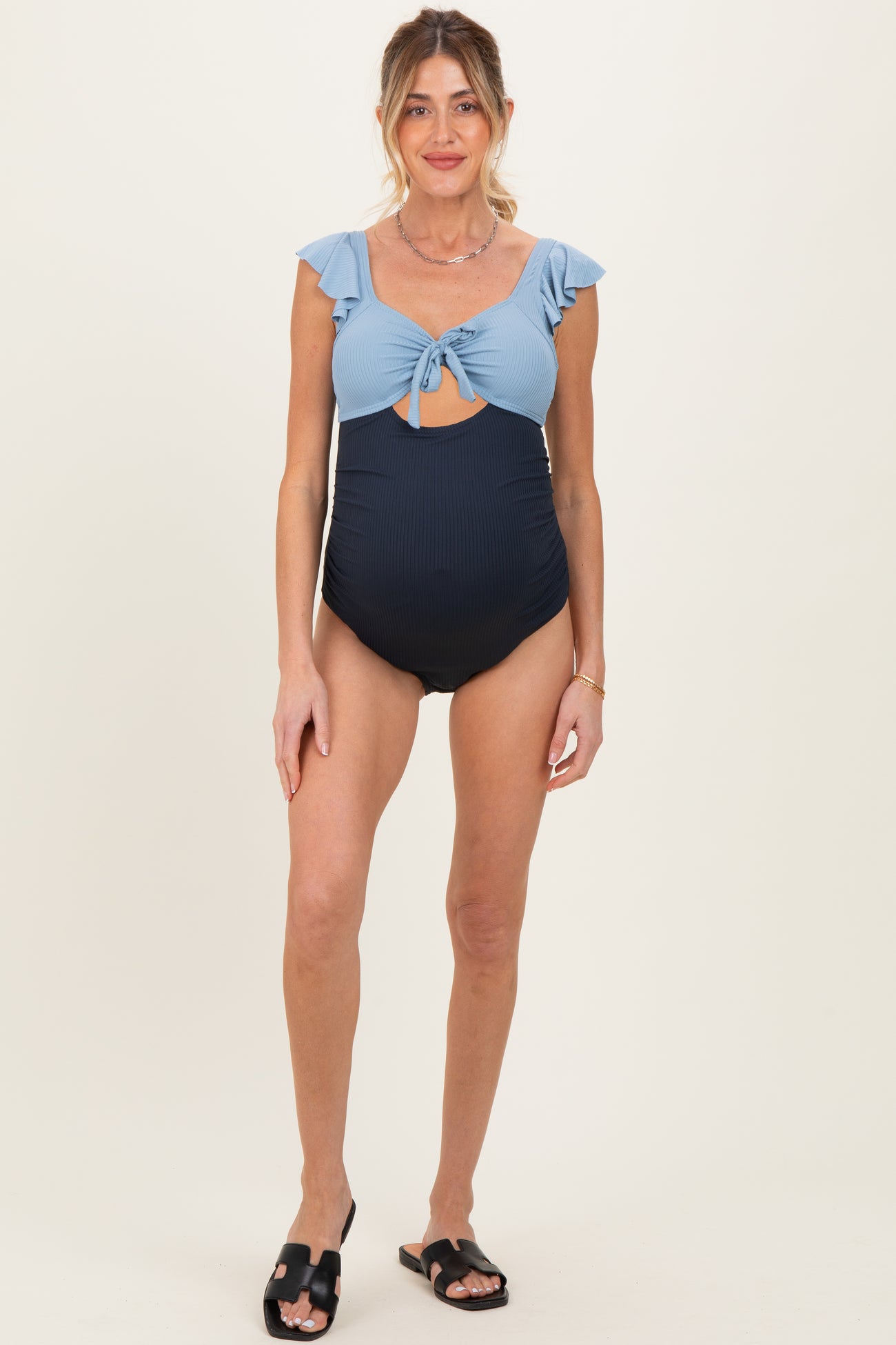 woman wearing a blue and navy striped maternity swimsuit with ruffle sleeves and a keyhole cutout