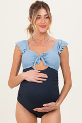 woman wearing a blue and navy maternity swimsuit with ruffle sleeves and a knot detail, holding her baby bump