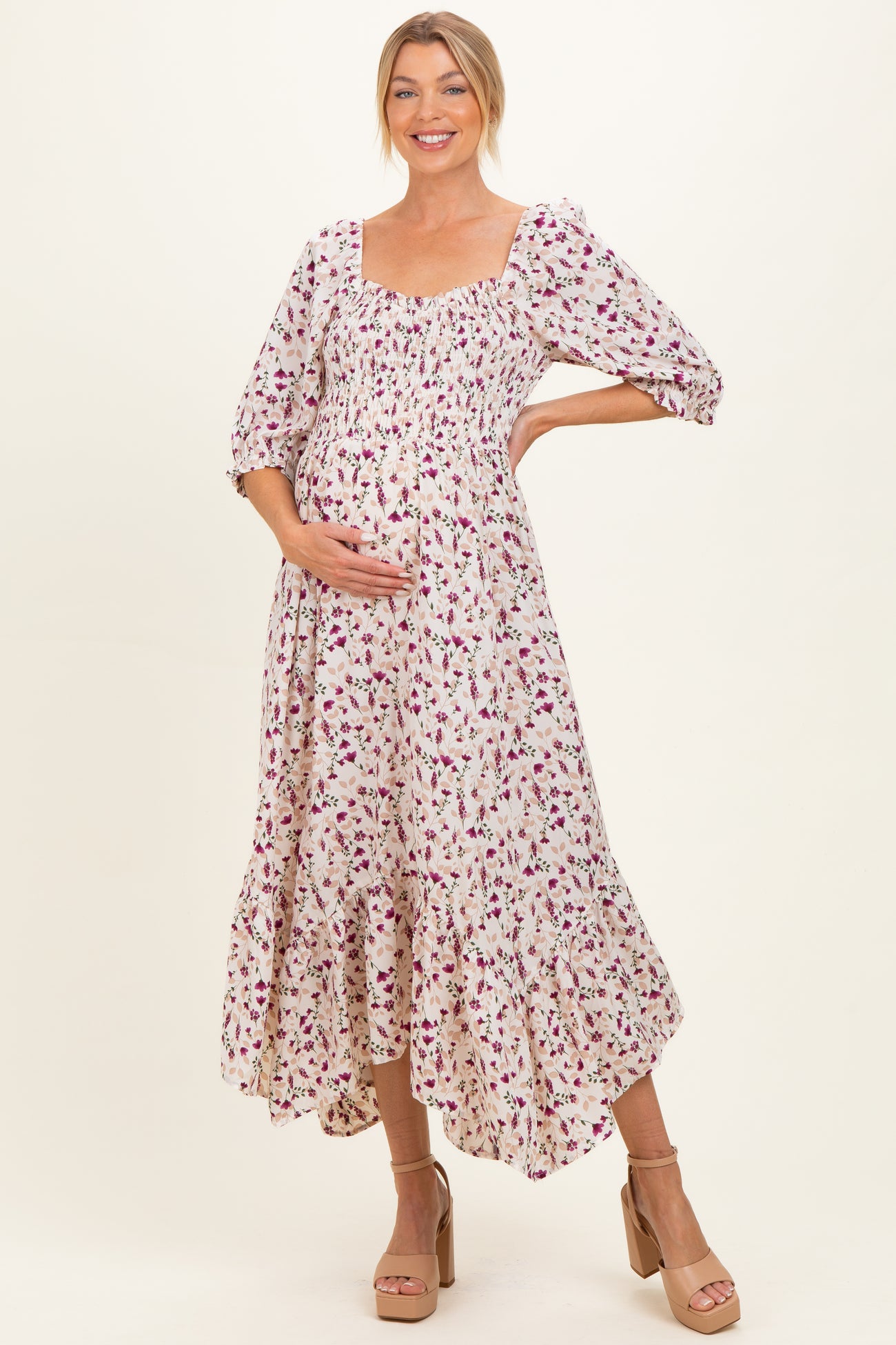 woman wearing a floral maternity midi dress with puff sleeves and a visible baby bump while smiling