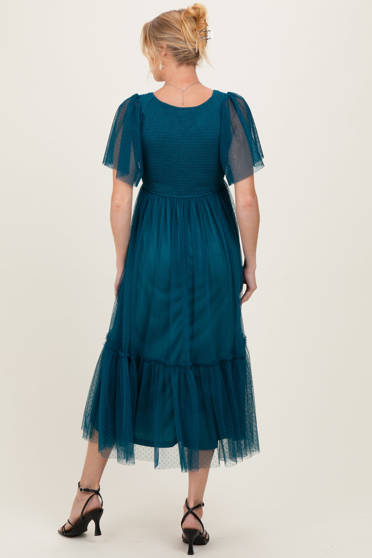 woman wearing a teal maternity dress with short puff sleeves and a tiered tulle hem, showing a baby bump from behind