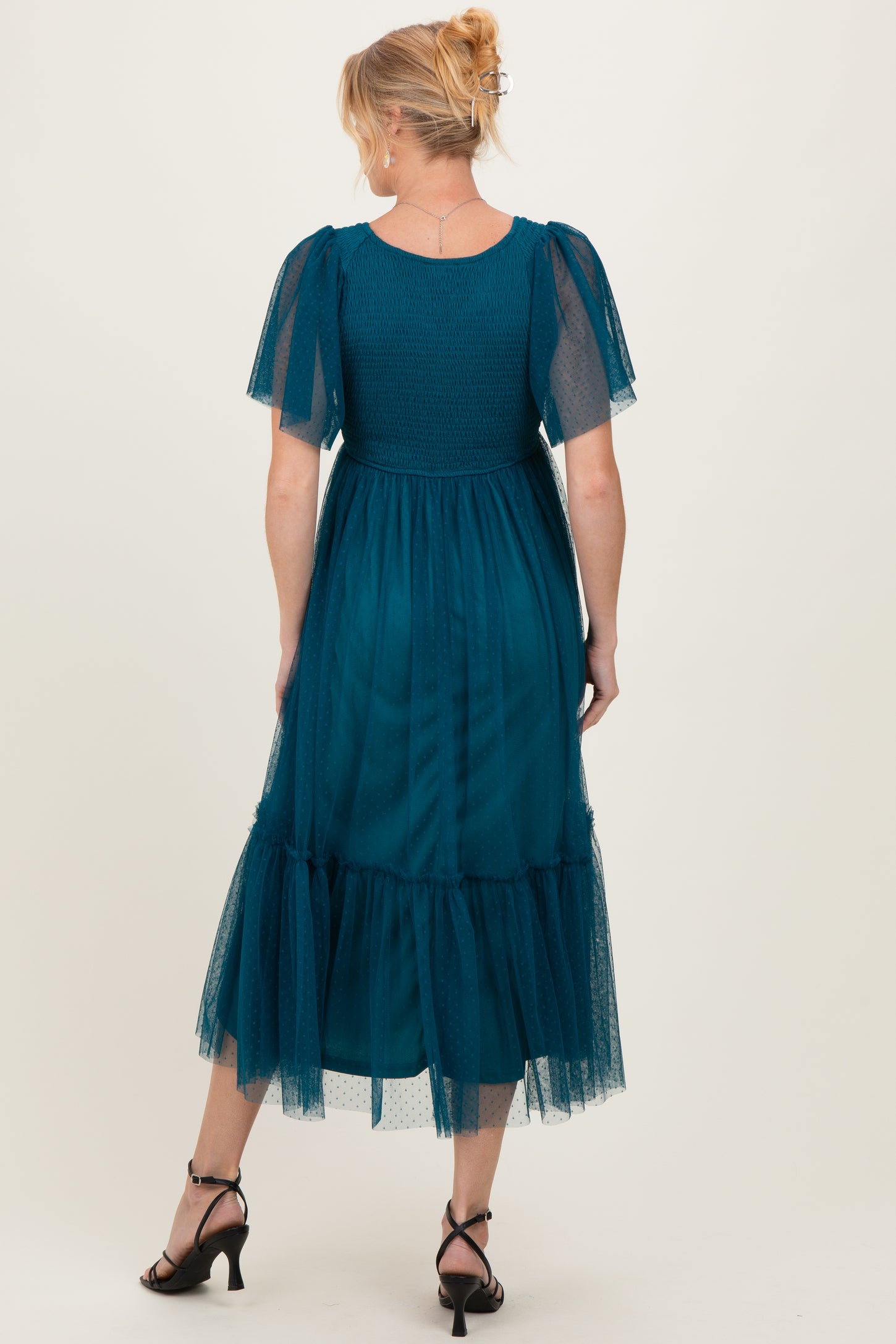 woman wearing a teal maternity dress with short puff sleeves and a tiered tulle hem, showing a baby bump from behind