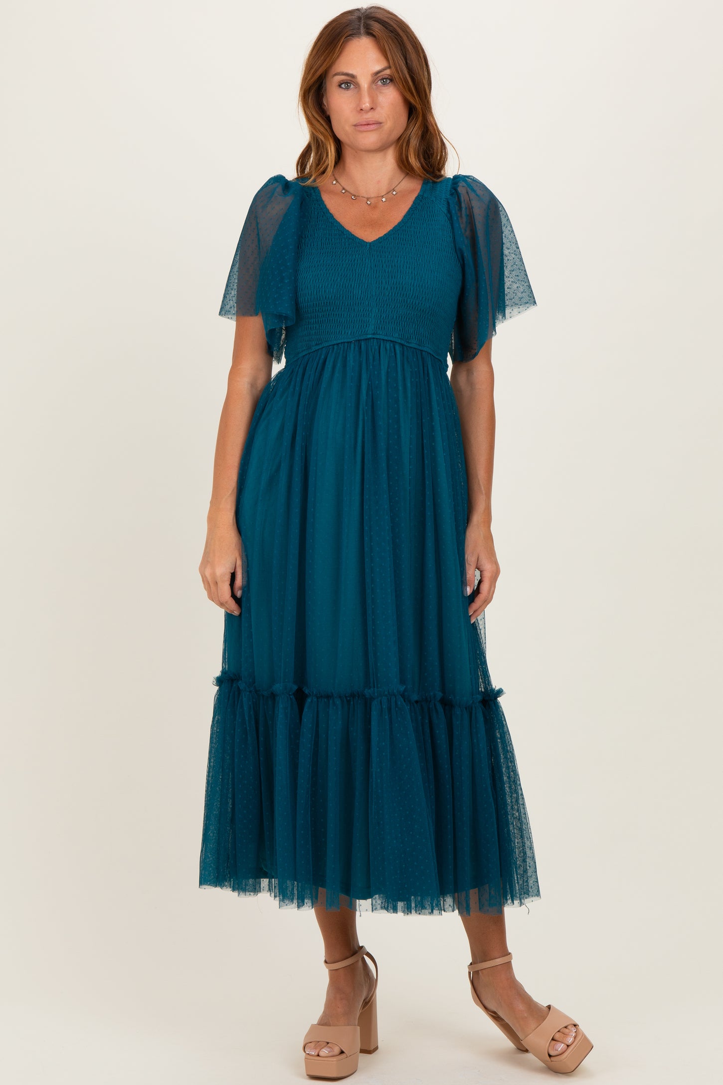woman wearing a teal midi dress with dotted sheer puff sleeves and a tiered tulle skirt, standing in beige block-heeled sandals