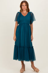 woman wearing a teal midi dress with dotted sheer puff sleeves and a tiered tulle skirt, standing in beige block-heeled sandals