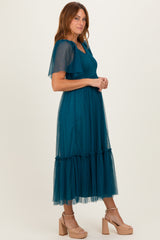 woman wearing a teal tulle midi dress with flutter sleeves and a ruffled hem, posing sideways against a neutral background