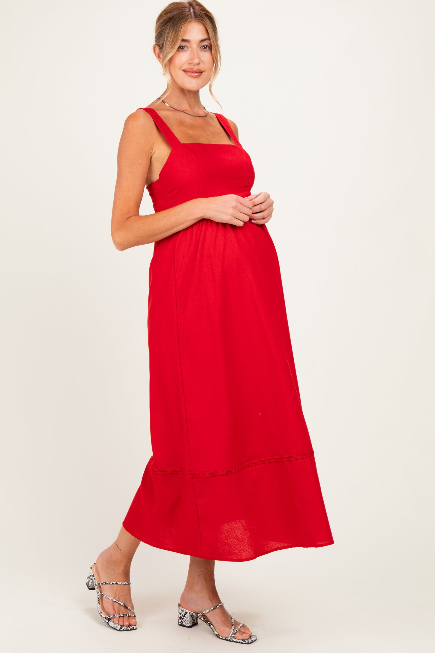 woman wearing a red maternity maxi dress with a square neckline and adjustable straps, showcasing her baby bump
