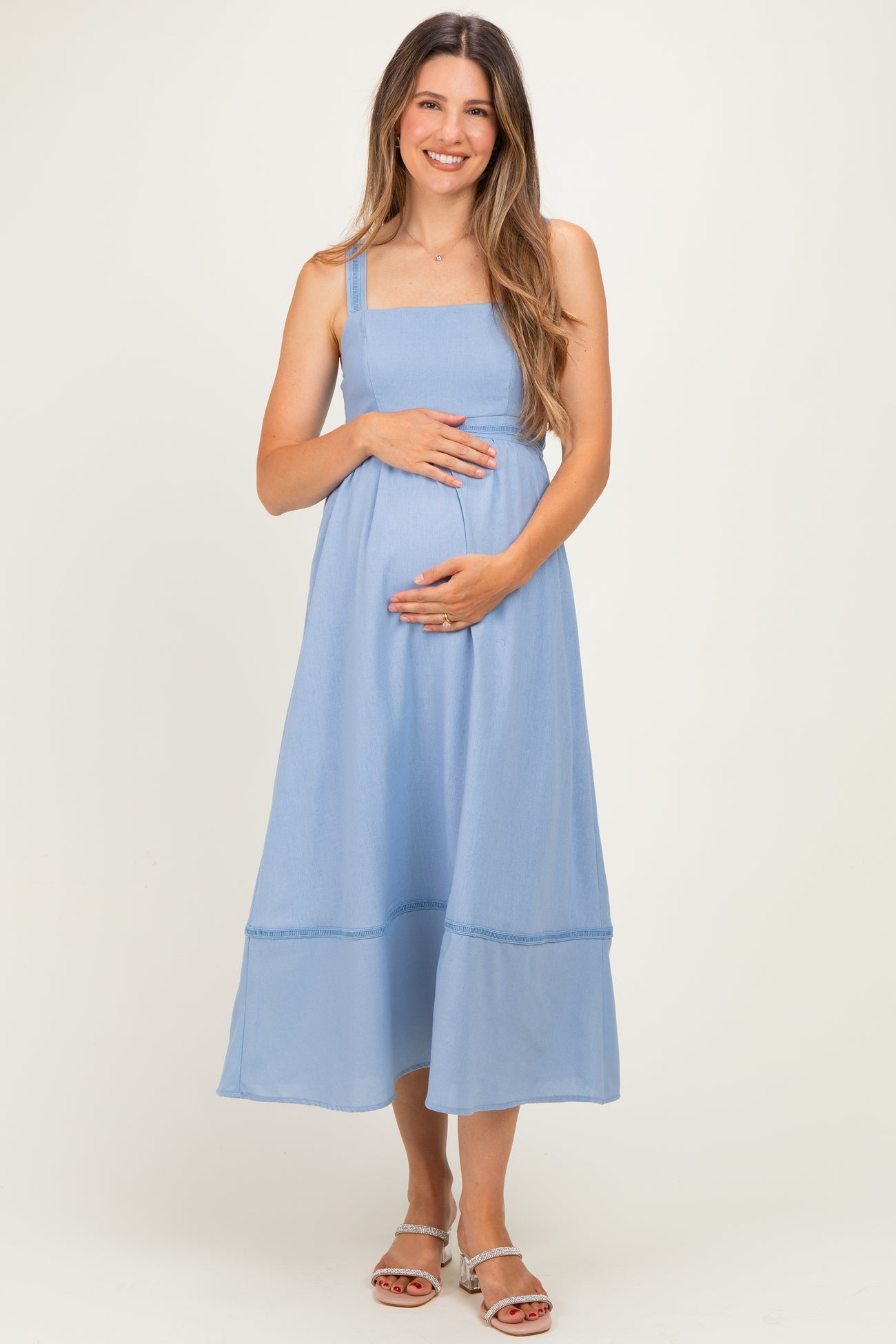 woman wearing a light blue maternity dress with a square neckline and holding her baby bump