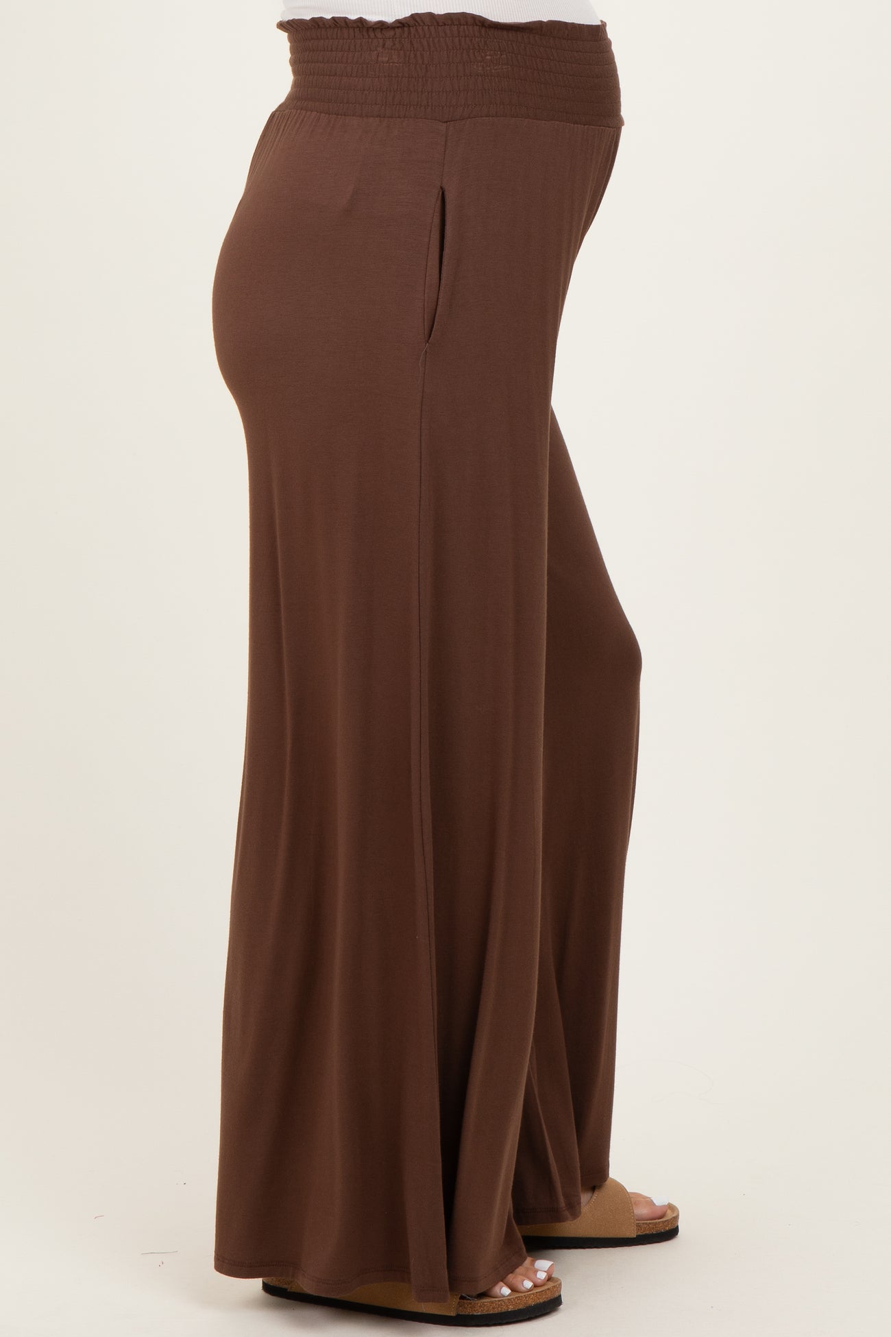 woman wearing brown maternity wide-leg pants with a smocked waistband and side pockets, showing a visible baby bump