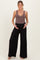 woman wearing a brown ribbed maternity tank top and black wide-leg maternity pants, holding her baby bump