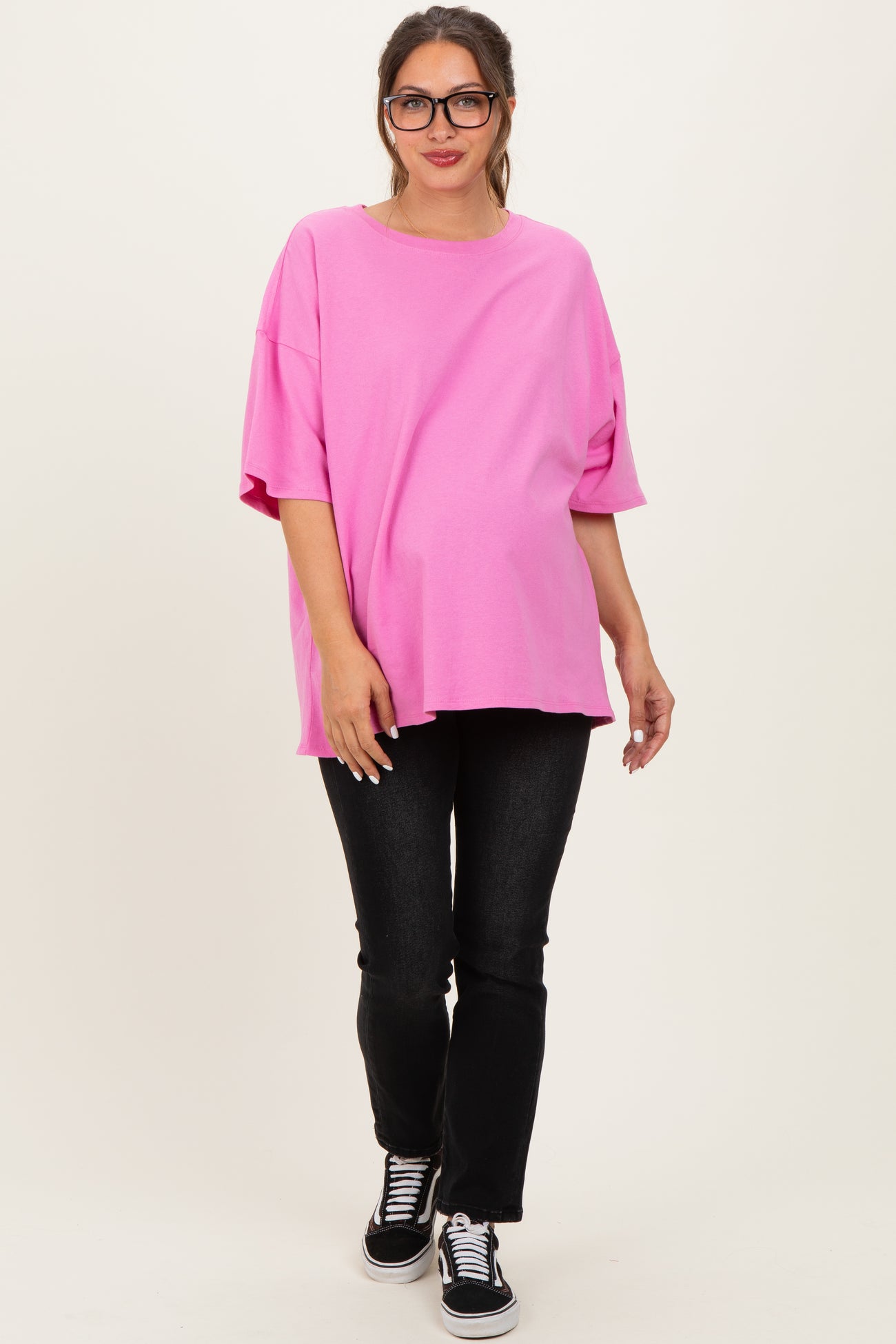 woman wearing a bright pink oversized maternity top with short sleeves and black skinny jeans, showing her baby bump