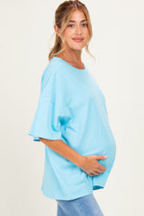 woman wearing a light blue oversized maternity top and holding her baby bump