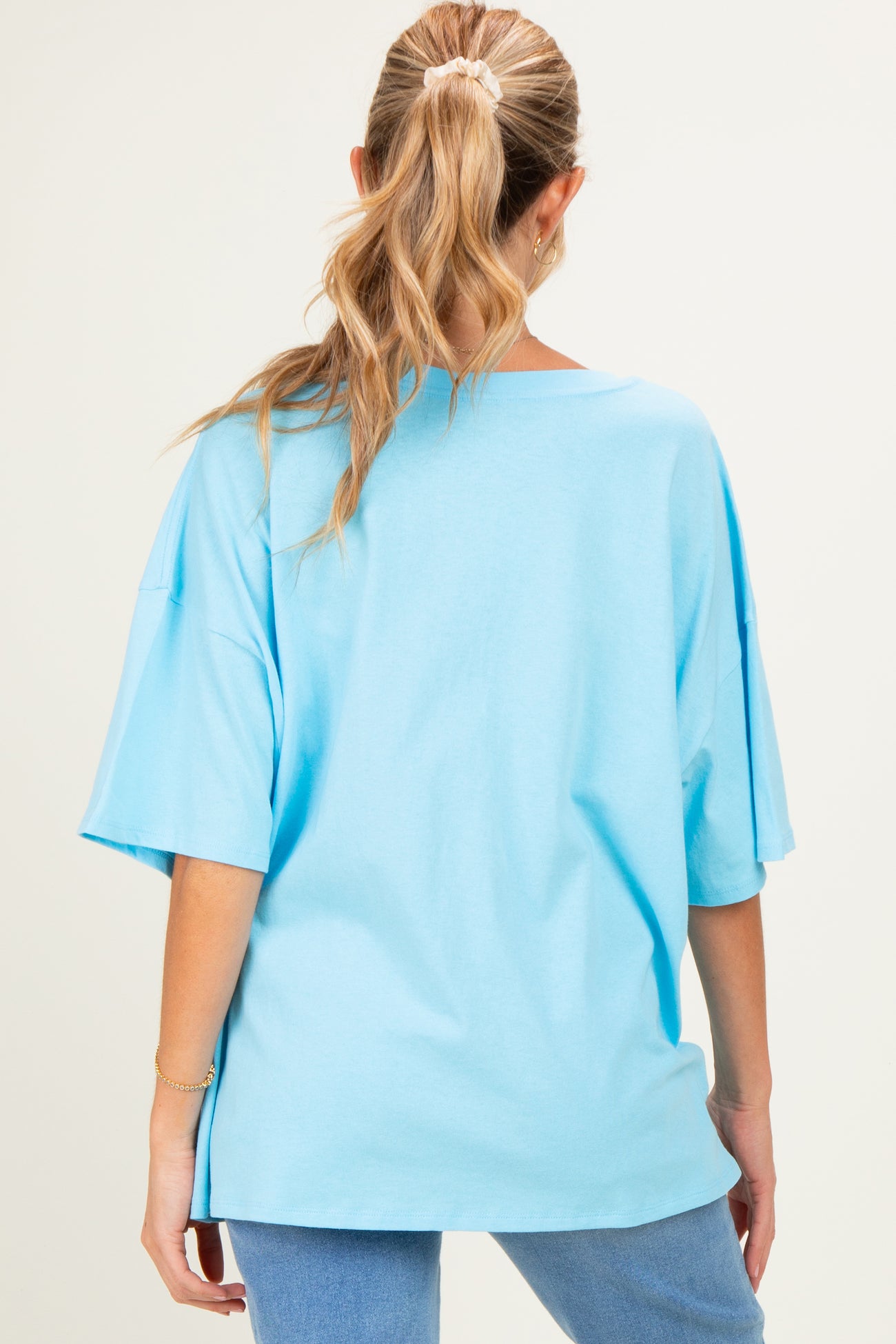 woman wearing a relaxed fit light blue maternity top with short sleeves, showing a simple back design