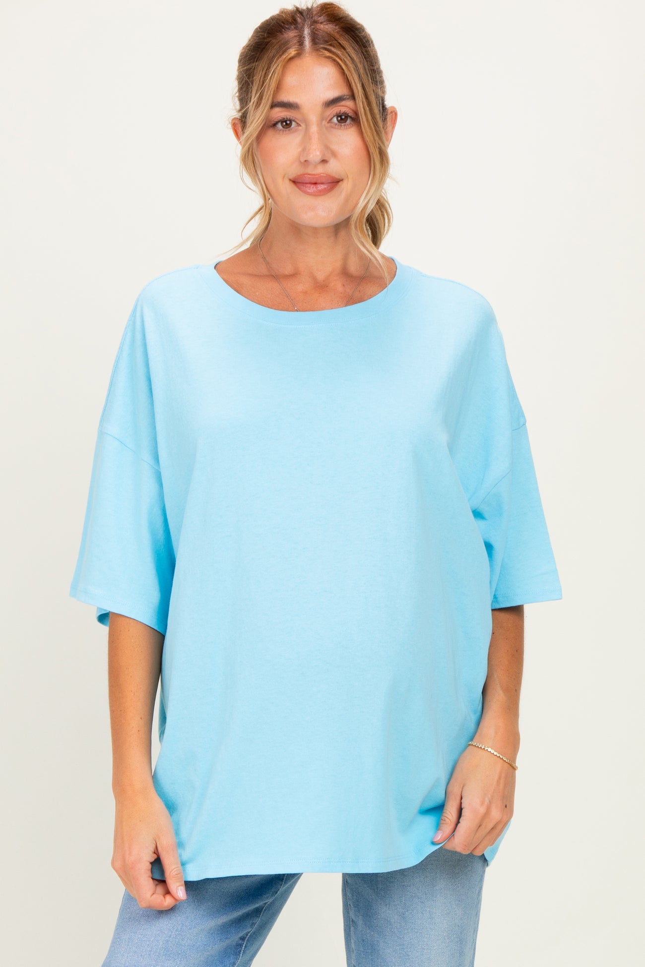 woman wearing a light blue oversized maternity top with short sleeves and a relaxed fit