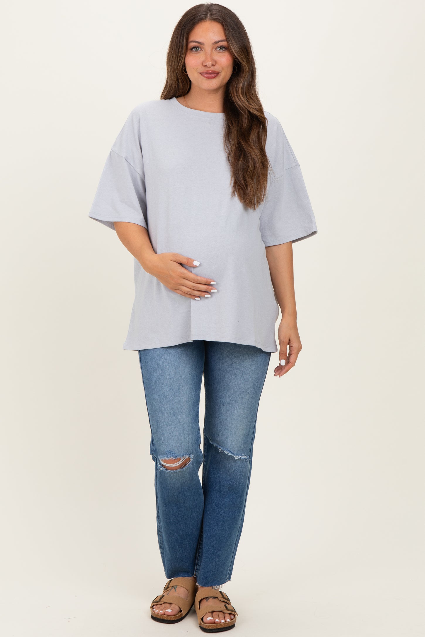 woman wearing a light gray oversized maternity t-shirt and holding her baby bump with distressed blue jeans
