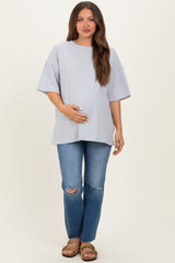 woman wearing a light gray oversized maternity t-shirt and holding her baby bump with distressed blue jeans