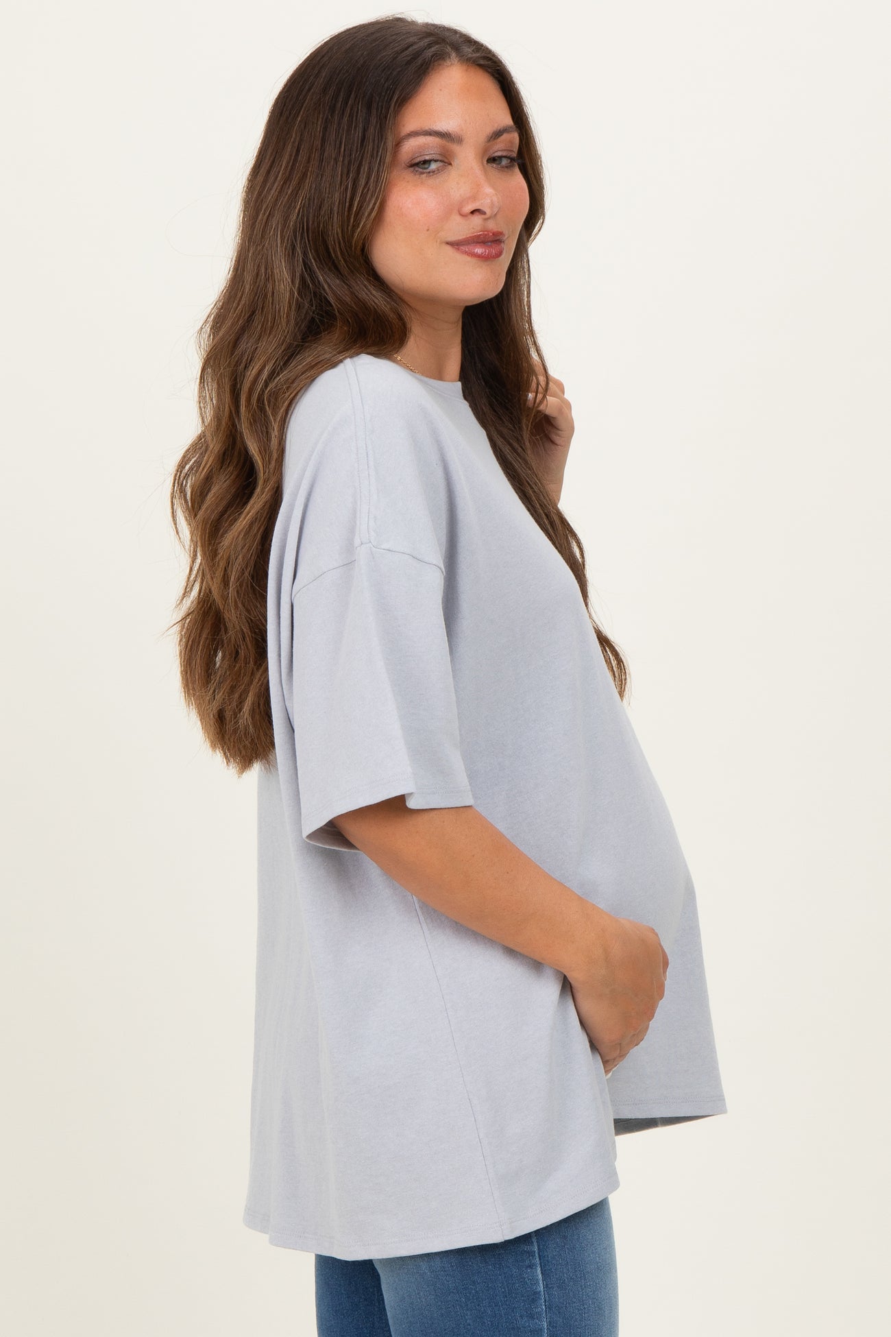 woman wearing a light gray oversized maternity t-shirt and holding her baby bump